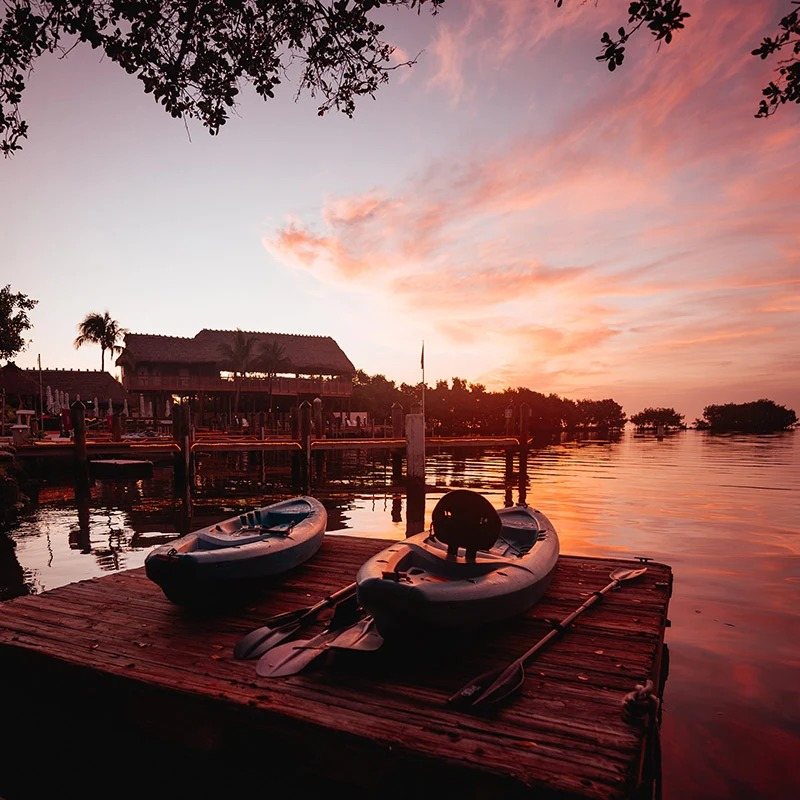 Two kayaks and their paddles resting on the wooden dock at the Snappers marina at sunset.
